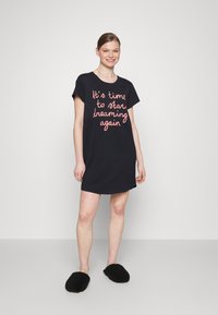 Granatowa sukienka t-shirtowa z krótkimi rękawami i luźnym krojem. Posiada różowy, ręcznie napisany tekst: "Czas znów zacząć marzyć". Czarny kapcie.