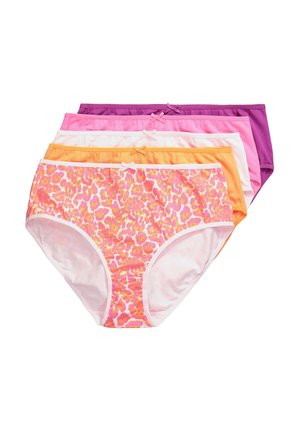 Plus-size vrouw draagt lichtroze beha met voorgevormde sluiting en hoogmodel slip, staand tegen een witte muur met hand op heup.