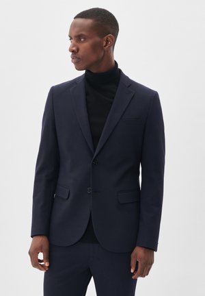 Navy blazer made of smooth fabric, notched lapels, single-button closure, two front pockets, fitted design, paired with a black turtleneck.
