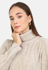 Pull en maille beige avec col roulé présentant des rayures texturées et un col côtelé, mis en valeur sur un fond neutre.