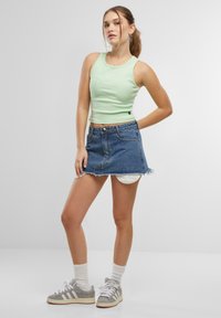 Light green fitted tank top with a round neckline, paired with a blue denim mini skirt featuring frayed hem and pockets. Gray sneakers with white stripes.