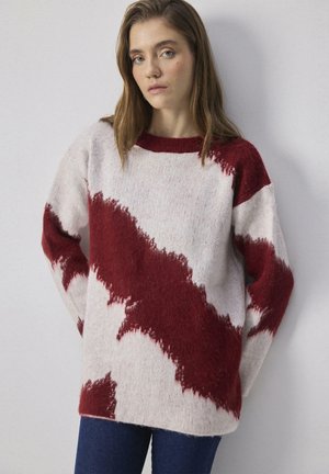 Maglione oversize in crema e rosso, con una texture morbida e pelosa e motivi astratti irregolari. Include un collo a giro e maniche lunghe.