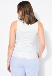 Witte, aansluitende tanktop met een geribbelde textuur, voorzien van brede schouderbanden. Gecombineerd met lichtblauwe verticaal gestreepte broeken.