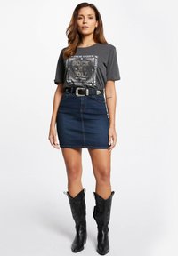 Grijze t-shirt met "Rock and Roll" graphic, gecombineerd met een donkere spijkerrok, zwarte leren cowboylaarzen met decoratieve stiksels.