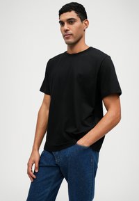 Μαύρη κοντομάνικη μπλούζα από βαμβάκι με λαιμόκοψη. Φορεμένη με μπλε τζιν παντελόνι, που διαθέτει πλαϊνές τσέπες και άνετη εφαρμογή.