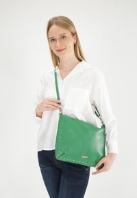 Groene leren handtas met zilveren studs langs de randen, voorzien van een afneembare schouderband. Gladde textuur, rechthoekige vorm.