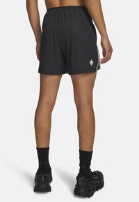 Mustad spordipüksid tekstuurse kangaga, kummist vöökohaga ja küljeaktsentidega. Kandmisel mustad spordijalatsid ja sokid.