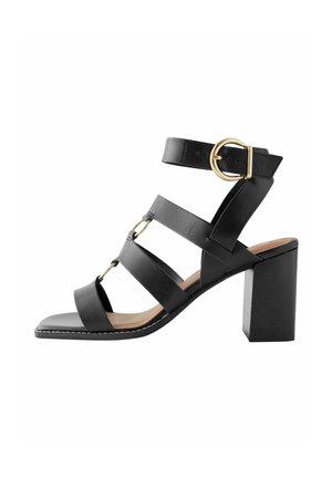 Sandale à talon en cuir noir avec bout carré, plusieurs lanières et une boucle dorée sur la lanière de la cheville. Style talon bloc.