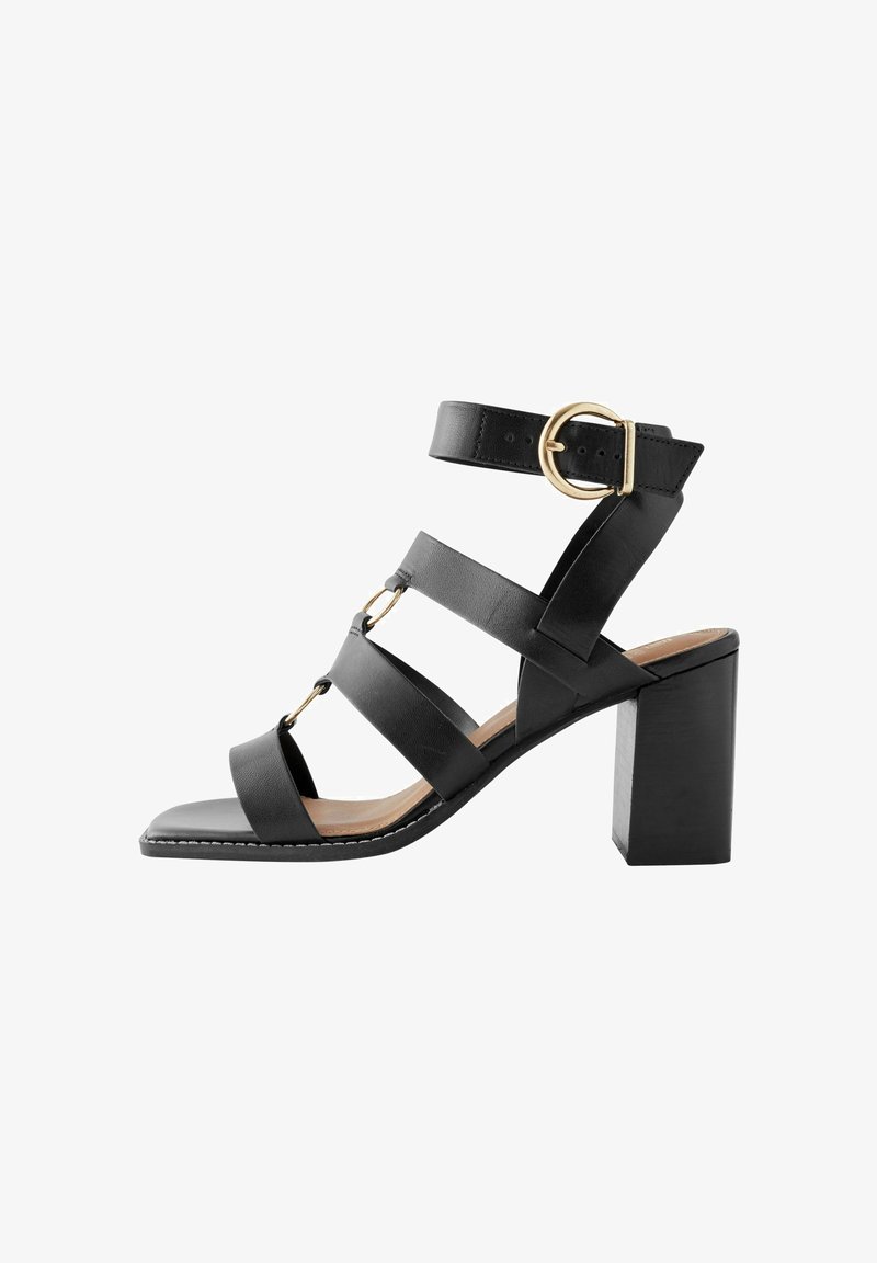 Sandale à talon en cuir noir avec bout carré, plusieurs lanières et une boucle dorée sur la lanière de la cheville. Style talon bloc.