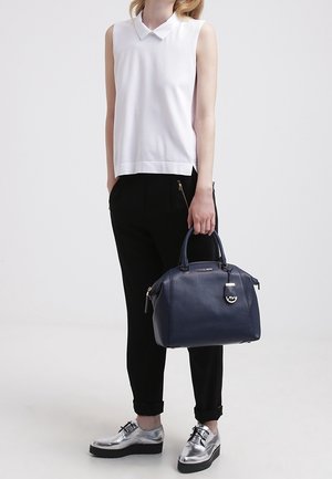 Borsa a mano in pelle blu mare con forma strutturata, manici doppi e accenti metallici. Abbinamento con un top bianco senza maniche, pantaloni neri e scarpe argentate.