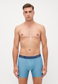 Boxers bleus clair avec une ceinture élastique navy affichant le texte "VOTRE SOUS-VÊTEMENT", présentant un design ajusté et une texture lisse.