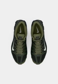 Σκούρο πράσινο αθλητικό παπούτσι Nike με δικτυωτό επάνω μέρος, παχύ μαύρο καουτσούκ σόλα και λευκή αχτίδα. Οι κορδόνες είναι ενσωματωμένες με επενδεδυμένο γιακά.