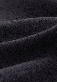 Zbliżenie na miękką, czarną tkaninę frotte z widocznymi pętelkami i zagięciami podkreślającymi jej teksturę i grubość.