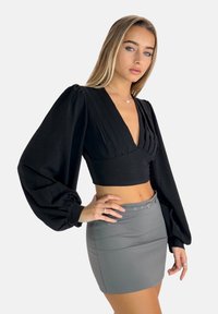 Blusa cropped nera con design plissettato e maniche voluminose, abbinata a una minigonna grigia aderente con cintura e dettagli di bottoni.