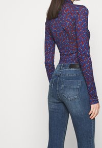 Camiseta de manga larga en azul oscuro con un patrón abstracto en rojo y azul claro, combinada con jeans ajustados de color azul desgastado que cuentan con bolsillos traseros.