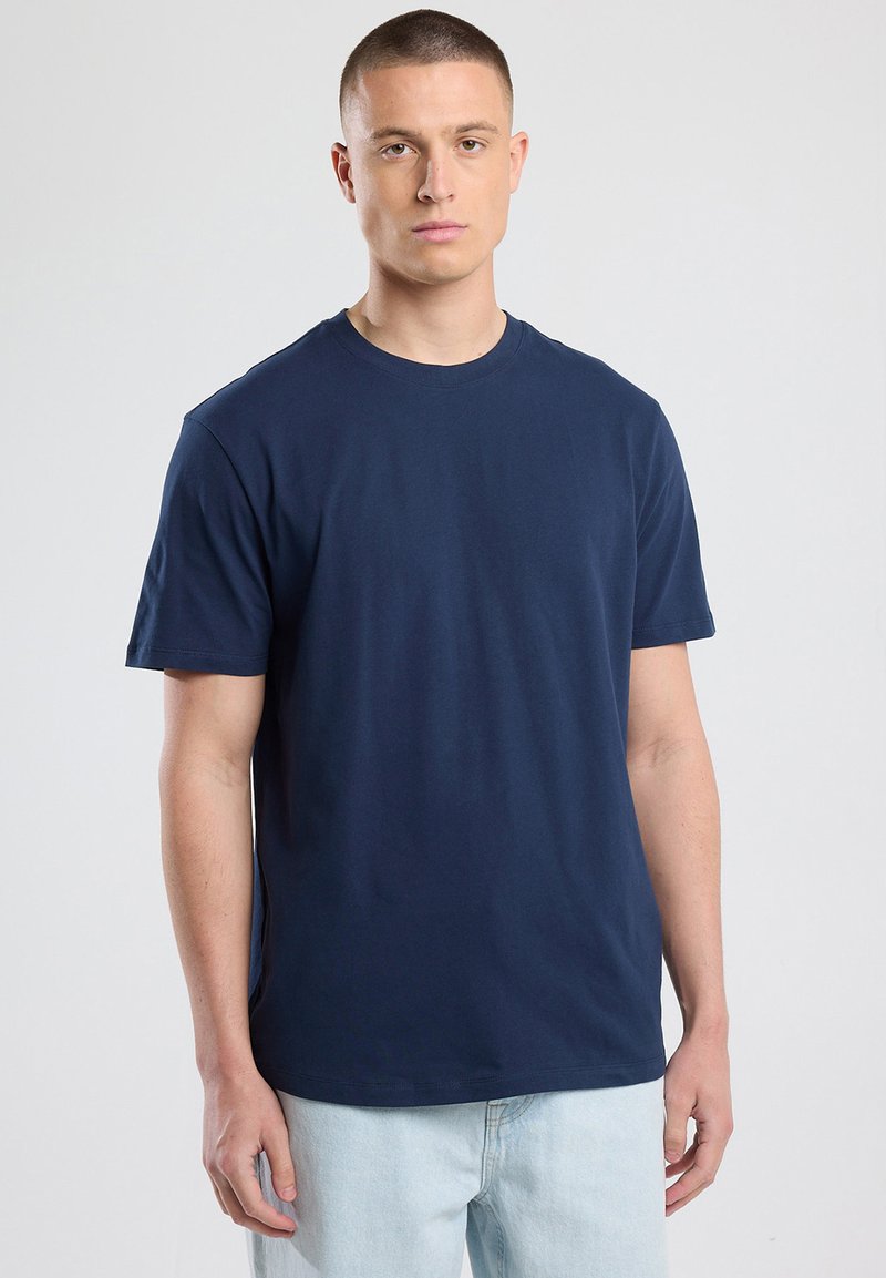 Tummansininen puuvillapaita, jossa on pyöreä pääntie, lyhyet hihat ja normaali istuvuus. Sileä rakenne, ei näkyviä kuvioita, käytetään vaaleiden farkkujen kanssa.