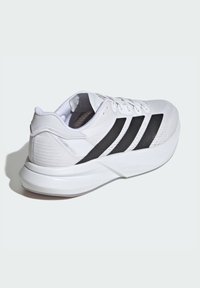 Baskets de sport blanches avec un design à trois rayures noires. Présentent une tige en maille texturée, un col rembourré et une semelle en caoutchouc blanc solide.