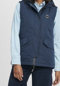 Marinblå väst med huva, tryckknappar, två framfickor och dragkedjestängning. Tillverkad av ett slätt, hållbart tyg.