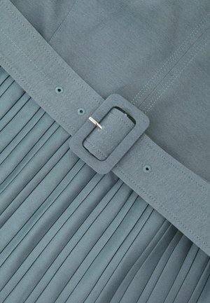 Falda gris plisada con un cinturón ancho de tela y una hebilla rectangular. El material es suave, con detalles cosidos y pliegues uniformemente espaciados.