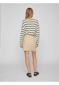 Beige kjol med bakficka och bälteshällor, kombinerad med en krämrandig, strukturerad långärmad skjorta. Sandaler fulländar outfiten.