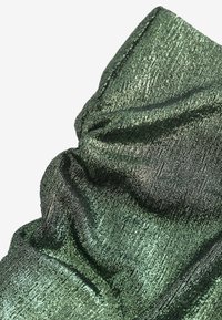 Metallisk grönt tyg med en texturerad, skrynklig yta. Har en glänsande lyster och varierande ljusreflektioner som framhäver dess vikta form.