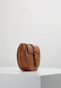 Braune Lederhandtasche mit runder Form, ausgestattet mit einem Klappverschluss und goldfarbenen Beschlägen. Texturierte Oberfläche mit kontrastierenden schwarzen Akzenten.