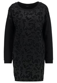 Czarna sukienka z górną częścią wykonaną z misternie haftowanej koronkowej tkaniny kwiatowej oraz jednolitą czarną dolną częścią, długimi rękawami i luźnym krojem z okrągłym dekoltem.