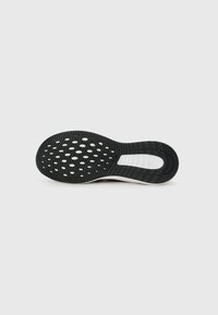 Semelle de chaussure en caoutchouc noir avec un motif de texture antidérapante, dotée d'une semelle intermédiaire blanche et d'une série de perforations circulaires pour la flexibilité.