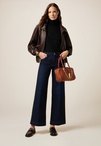 Chaqueta de cuero marrón, suéter negro de cuello alto, jeans oscuros de pierna ancha, mocasines negros y un bolso marrón con detalle de cadena dorada.