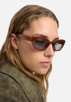 Brązowe, kanciaste okulary przeciwsłoneczne z przezroczystymi brązowymi oprawkami i szarymi soczewkami, charakteryzujące się minimalnym detalem i eleganckim wzornictwem.