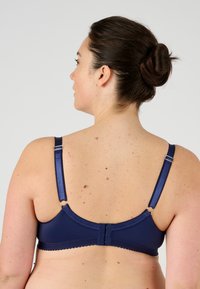 Sostenedor azul marino con tela suave, tirantes ajustables y ribete en forma de ola. Incluye cierre de gancho y ojo y acentos metálicos redondos.