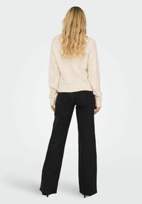 Pull en maille torsadée crème avec un motif texturé, associé à un pantalon noir taille haute à jambes larges, doté de poches arrière et d'une finition douce.