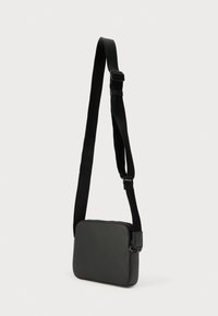 Μαύρο συνθετικό τσαντάκι χιαστί με υφή, ορθογώνιο σχήμα, ρυθμιζόμενο λουρί και κλείσιμο με φερμουάρ. Απλός και συμπαγής σχεδιασμός.