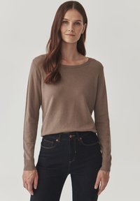 Bruine lange mouwen trui van zacht breiwerk, met een ronde halslijn en geribde manchetten, gecombineerd met donkerblauwe jeans.