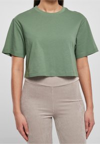 Olivengrøn cropped T-shirt med korte ærmer, rund halsudskæring og blød, glat tekstur. Kombineret med lysebeige ribbede bukser.