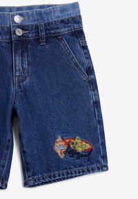 Pantalones cortos de mezclilla en azul oscuro con un cierre de dos botones, bolsillos delanteros y un parche bordado colorido con acentos en naranja y verde.