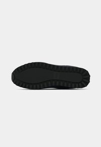 Semelle de chaussure en caoutchouc noir robuste avec un motif profond et le nom de la marque embossé au centre sur fond gris clair.