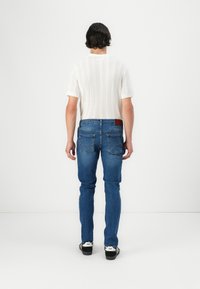 Hvit kortermet, ribbestrikket skjorte kombinert med blå denimjeans. Jeansene har en lapp på baklivet og klassiske lommer.