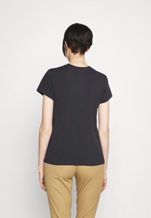 T-shirt gris foncé avec un col rond et des manches courtes, présentant une texture lisse. Porté avec un pantalon beige, affichant un design simple.