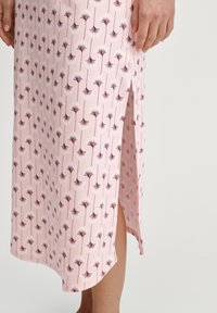 Lichtroze midi-rok met een donkerpaarse bloemenprint en een zijsplit, gedragen door een persoon met één hand ontspannen aan de zij.