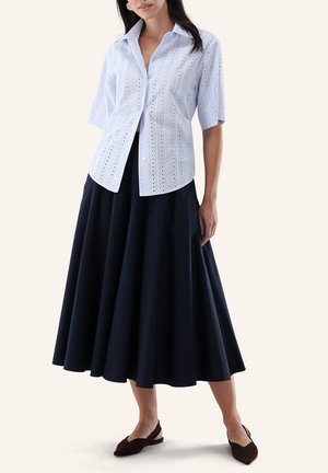 Woman wearing a light blue eyelet short-sleeve button-up shirt, navy wide midi skirt, and dark brown flat shoes.