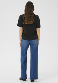 T-shirt nero in cotone con maniche corte, abbinato a jeans a vita alta blu a gamba larga e stivali neri con tacco, visto da dietro.