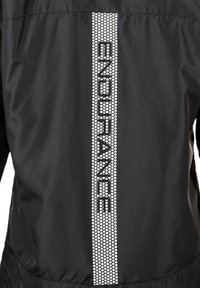 Cazadora negra con un tirante de patrón hexagonal reflectante y el texto "ENDURANCE" en blanco en el centro de la parte posterior. Textura de tela suave.