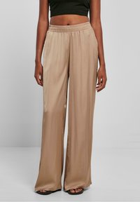 Beige, wijde broek van gladde, glanzende stof met een elastische tailleband en zijzakken, die een losse, vloeiende silhoutte creëert.