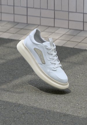 Hvit lær sneakers med en glatt finish, som har en polstret krage, flate snøring, perforeringer på tåen og en kremfarget såle.