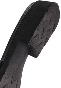 Semelle épaisse noire de chaussure plateforme avec une surface en caoutchouc texturée présentant des motifs ondulés sur la face inférieure.