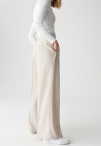 Beige wijde broek van gestreepte stof met zijzakken, gecombineerd met witte schoenen. Het ontwerp heeft een ontspannen silhouet.