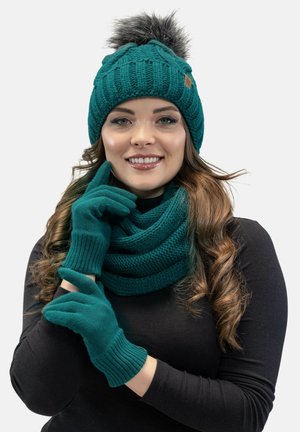 Gorro de punto en color verde azulado con un pompón de peluche sintético, guantes a juego en verde azulado y una bufanda gruesa. Presenta patrones acanalados y una textura suave.