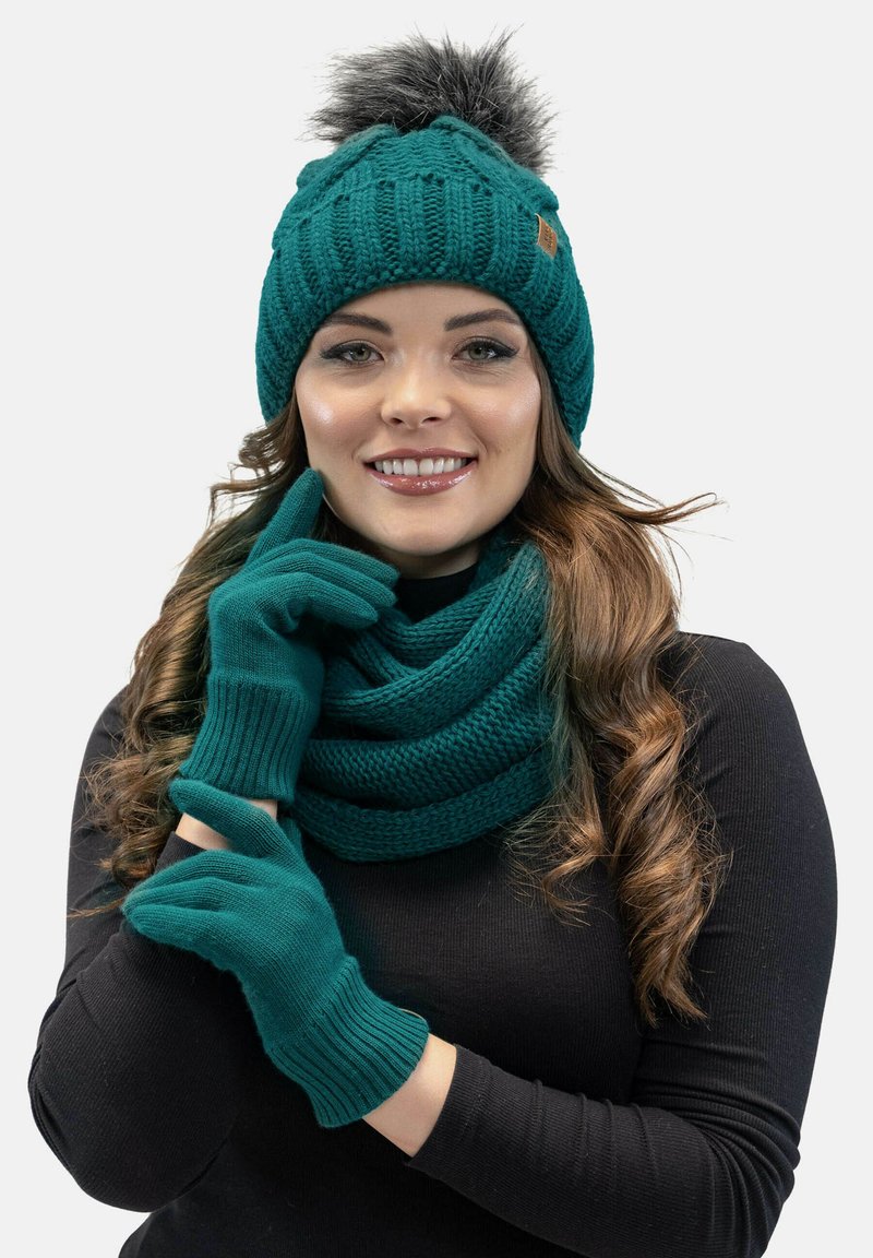 Gorro de punto en color verde azulado con un pompón de peluche sintético, guantes a juego en verde azulado y una bufanda gruesa. Presenta patrones acanalados y una textura suave.