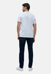 Weißes Baumwoll-T-Shirt mit kurzen Ärmeln, kombiniert mit dunkelblauen Jeans und weißen Sneakern. Ansicht von hinten, die ein einfaches Design zeigt.